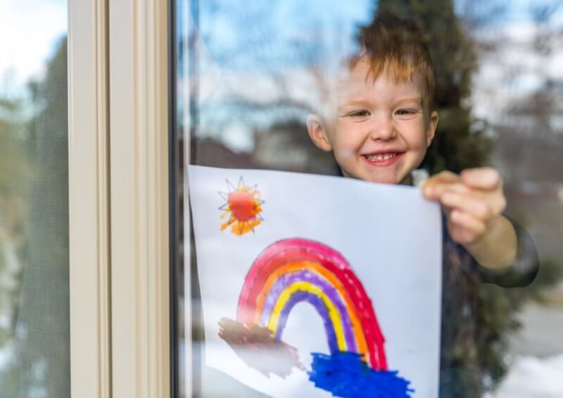 A young boy putting a painted rainbow on the window